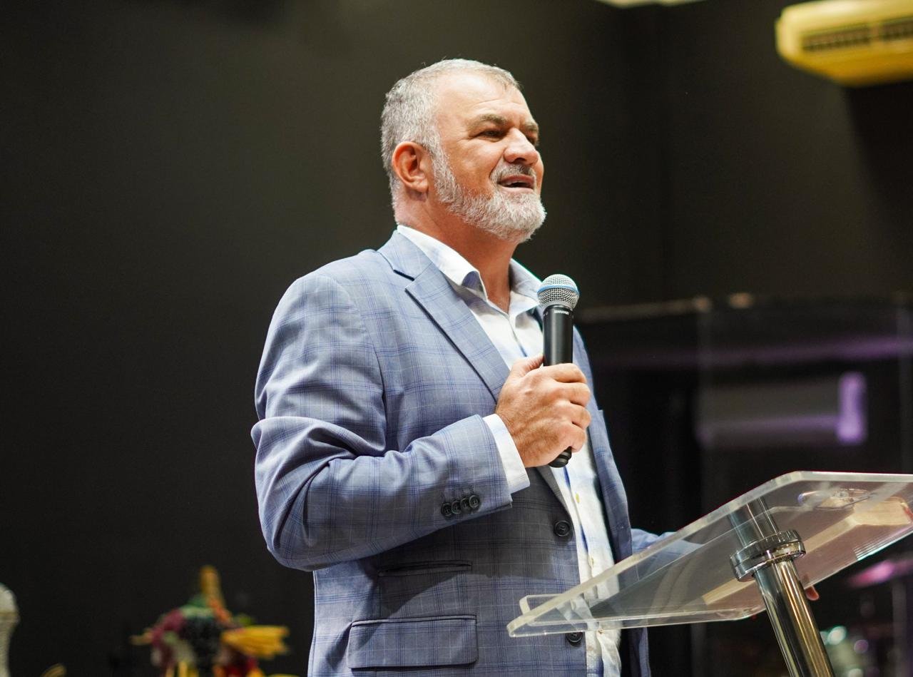 Pastor Tilica pregando, microfone na mão, durante um culto